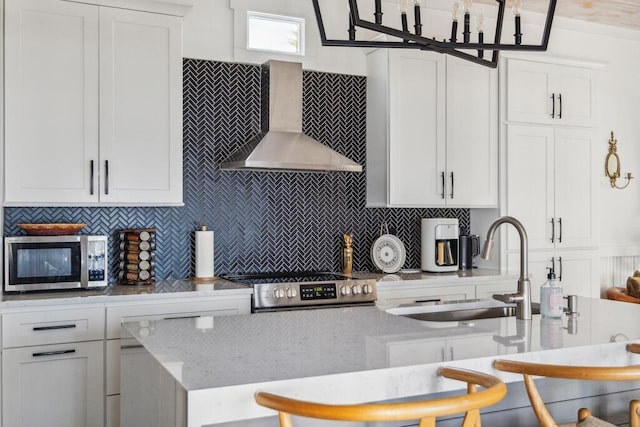 kitchen with stainless steel appliances, wall chimney exhaust hood, a sink, backsplash, and white cabinets