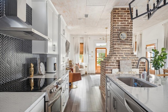 kitchen featuring wall chimney exhaust hood, a sink, appliances with stainless steel finishes, dark wood-style flooring, and light stone countertops