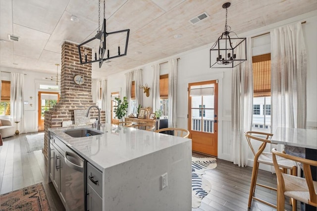 kitchen with a chandelier, a sink, dark wood-type flooring, stainless steel dishwasher, and an island with sink