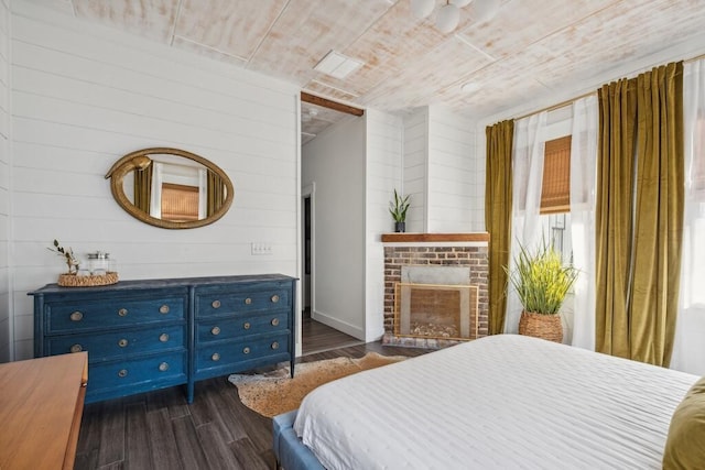 bedroom with dark wood-style flooring, a fireplace, and wooden walls