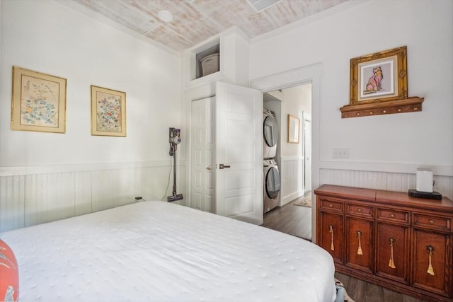 bedroom featuring estacked washer and dryer, dark wood-type flooring, and wainscoting