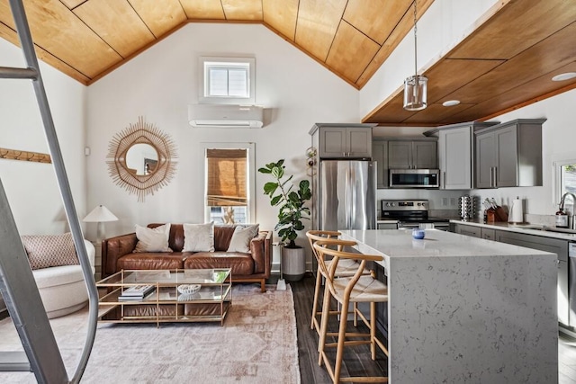 kitchen featuring stainless steel appliances, gray cabinetry, a wall unit AC, light stone counters, and a sink