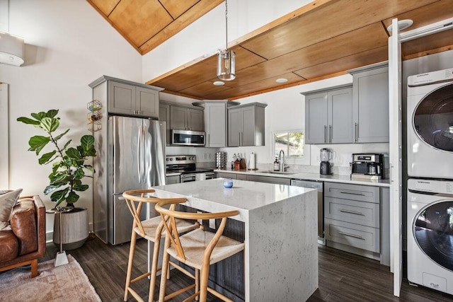 kitchen featuring stainless steel appliances, gray cabinetry, wooden ceiling, stacked washer and clothes dryer, and a sink