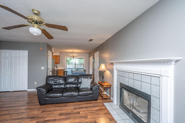 living area with a fireplace, a textured ceiling, ceiling fan with notable chandelier, wood finished floors, and visible vents