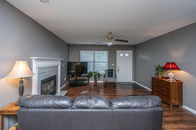 living room with wood finished floors, baseboards, a textured ceiling, a tiled fireplace, and a ceiling fan