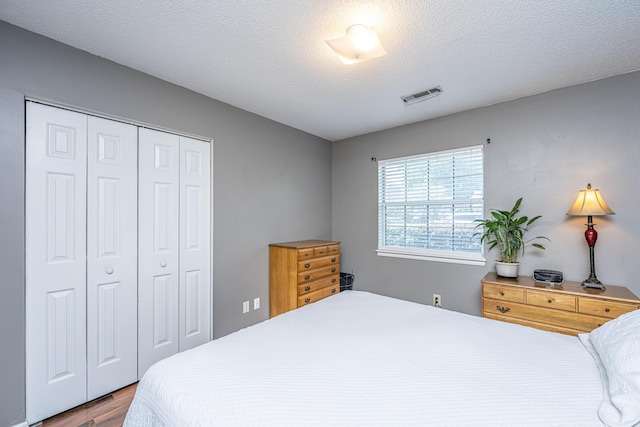 bedroom featuring a textured ceiling, visible vents, wood finished floors, and a closet