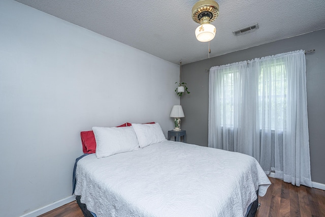bedroom with a textured ceiling, baseboards, visible vents, and wood finished floors
