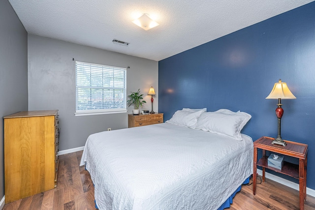 bedroom with baseboards, a textured ceiling, wood finished floors, and visible vents