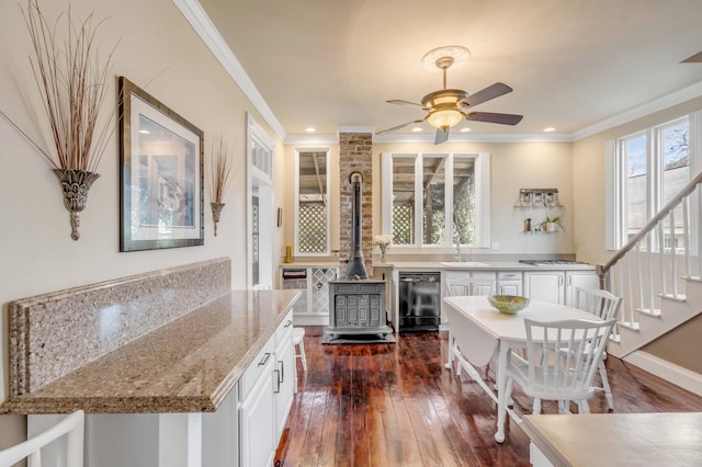 kitchen with dishwasher, white cabinetry, light stone counters, and a wood stove