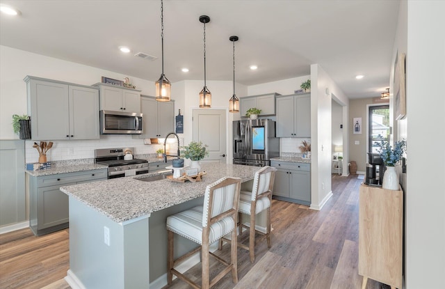 kitchen featuring stainless steel appliances, a kitchen breakfast bar, an island with sink, light hardwood / wood-style flooring, and decorative backsplash