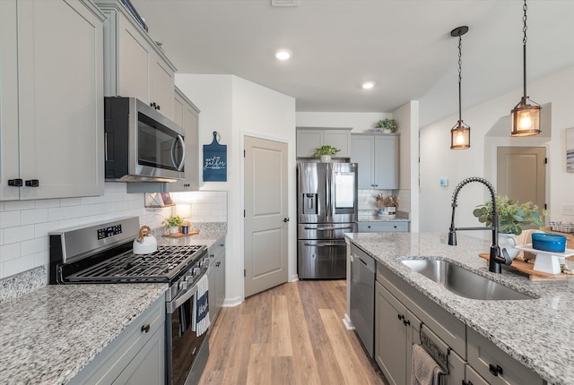 kitchen with light stone counters, appliances with stainless steel finishes, decorative light fixtures, sink, and light hardwood / wood-style flooring