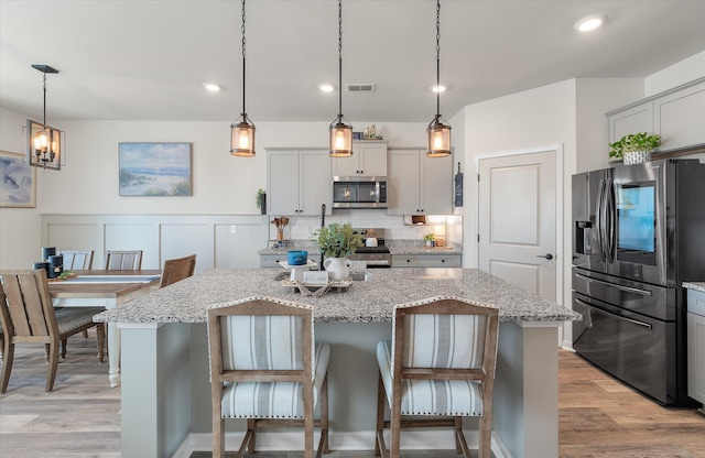 kitchen with light hardwood / wood-style floors, appliances with stainless steel finishes, a center island, and decorative light fixtures