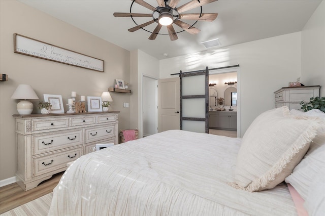 bedroom featuring light hardwood / wood-style floors, a barn door, ceiling fan, and ensuite bathroom