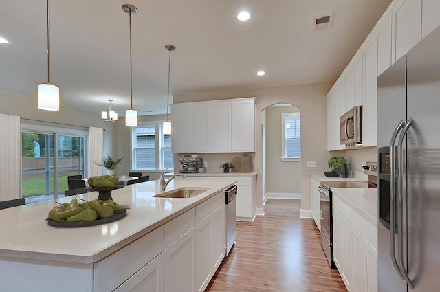 kitchen featuring appliances with stainless steel finishes, decorative light fixtures, white cabinetry, sink, and a center island with sink