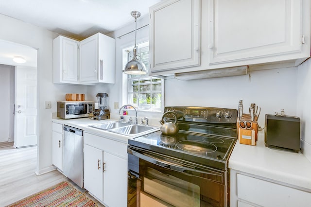 kitchen featuring appliances with stainless steel finishes, sink, pendant lighting, light hardwood / wood-style flooring, and white cabinetry