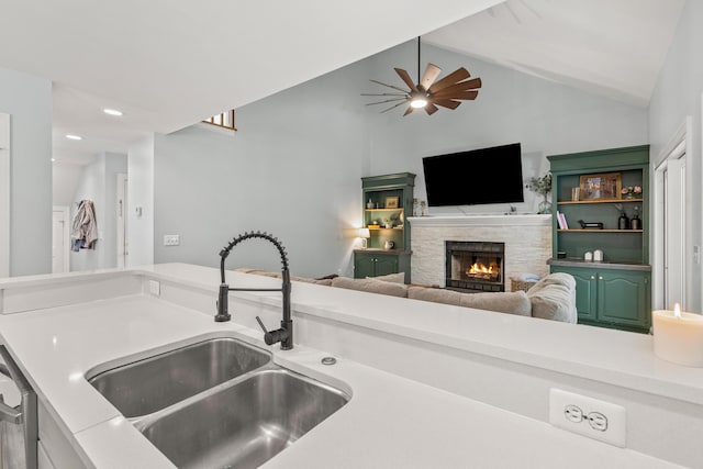 kitchen featuring vaulted ceiling, ceiling fan, sink, dishwasher, and a fireplace