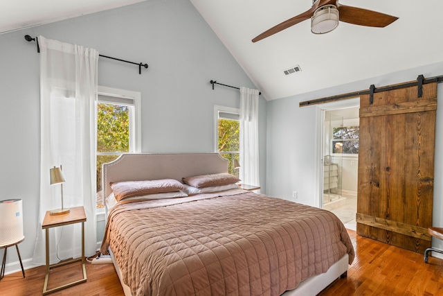 bedroom with hardwood / wood-style floors, ceiling fan, a barn door, and ensuite bath