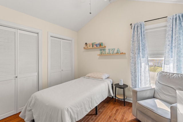 bedroom with light hardwood / wood-style floors, lofted ceiling, and two closets