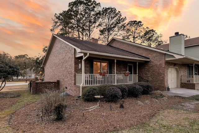 view of front of house featuring covered porch, brick siding, a chimney, and a garage