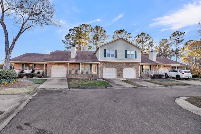 split level home featuring an attached garage, covered porch, brick siding, driveway, and a chimney