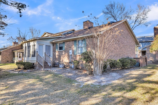 rear view of property featuring brick siding, a chimney, and a lawn