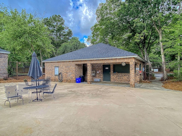 exterior space featuring a patio area, a shingled roof, fence, and brick siding