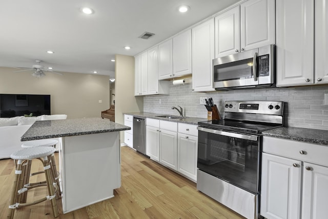 kitchen with white cabinetry, stainless steel appliances, a kitchen island, light hardwood / wood-style flooring, and sink