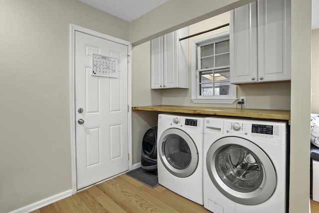 clothes washing area with light wood-type flooring, cabinets, and washer and clothes dryer