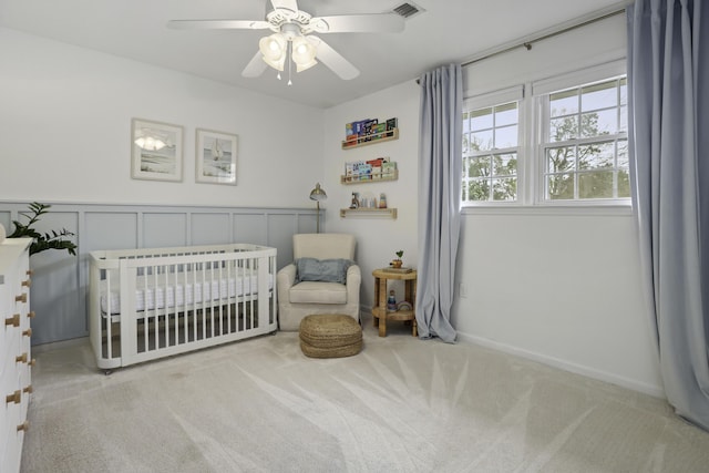 bedroom featuring ceiling fan, light colored carpet, and a crib