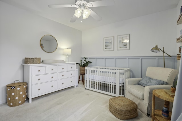 carpeted bedroom featuring ceiling fan and a nursery area