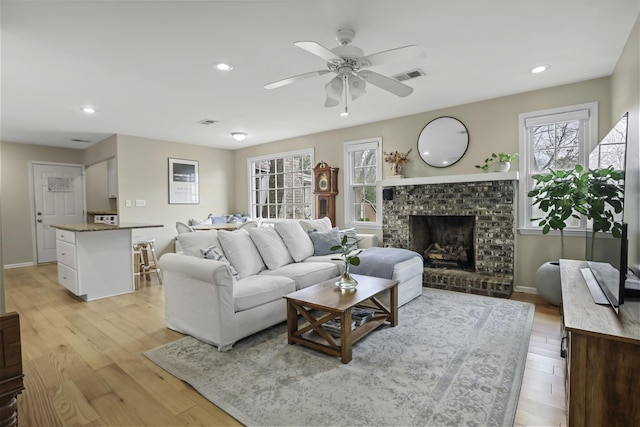 living room with ceiling fan, a brick fireplace, and light hardwood / wood-style floors