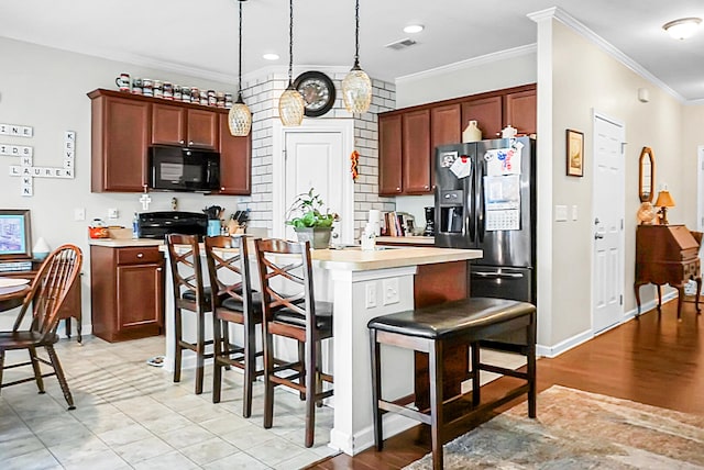 kitchen featuring a breakfast bar, hanging light fixtures, ornamental molding, and black appliances