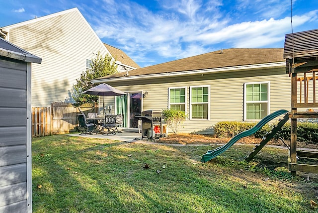 rear view of property featuring a playground, a patio area, and a lawn