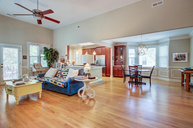 living area featuring light wood-style floors, a decorative wall, ceiling fan with notable chandelier, and visible vents