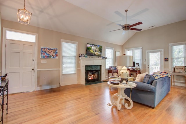 living room with a premium fireplace, ceiling fan with notable chandelier, baseboards, lofted ceiling, and light wood-type flooring
