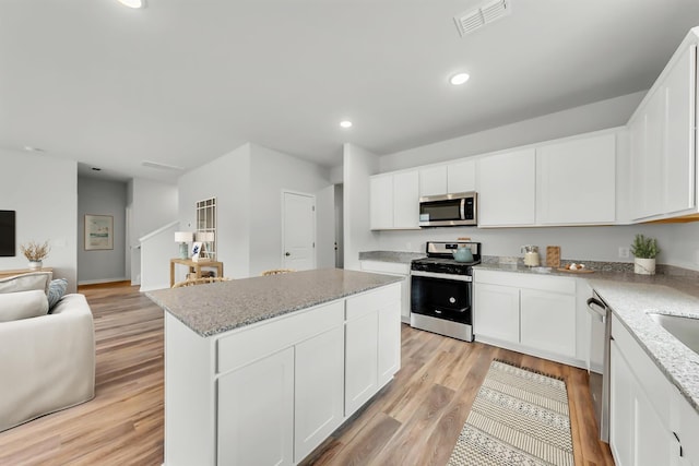 kitchen with visible vents, a kitchen island, open floor plan, stainless steel appliances, and light wood-style floors