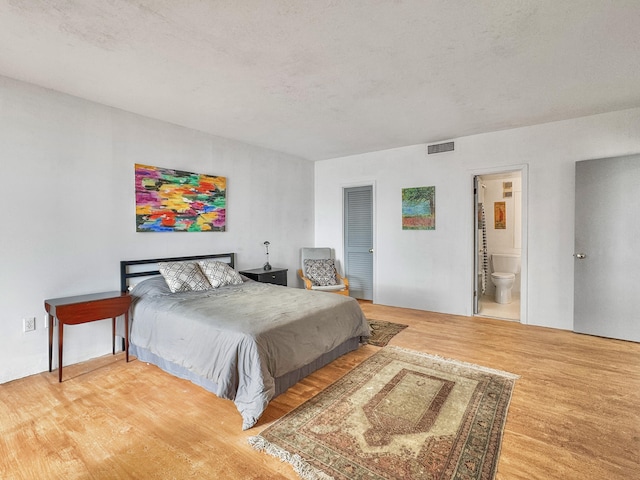 bedroom with ensuite bath, wood-type flooring, and a textured ceiling