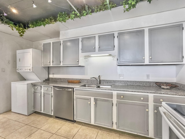 kitchen featuring stainless steel dishwasher, gray cabinetry, sink, light tile patterned floors, and stacked washer / drying machine