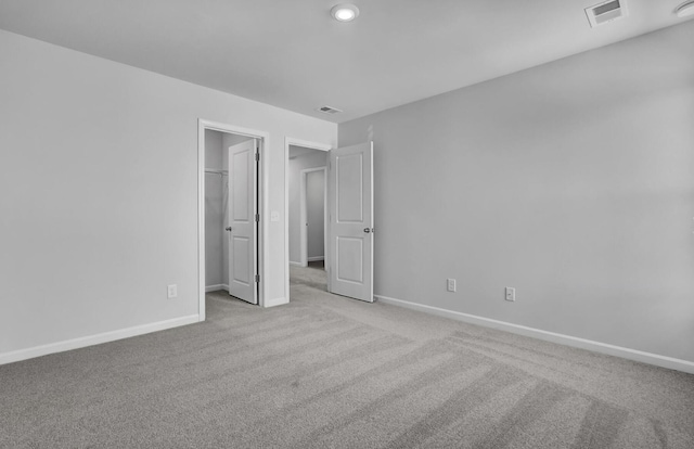 unfurnished bedroom with light carpet, baseboards, and a walk in closet