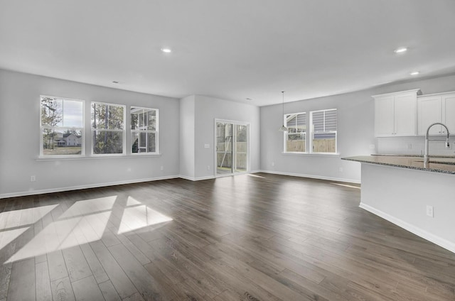 unfurnished living room with a sink, dark wood finished floors, recessed lighting, and baseboards