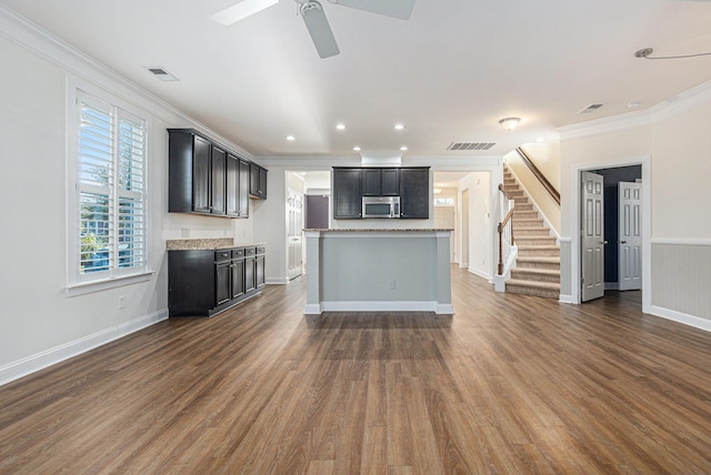 kitchen with ceiling fan, dark wood-type flooring, light stone counters, a center island, and ornamental molding