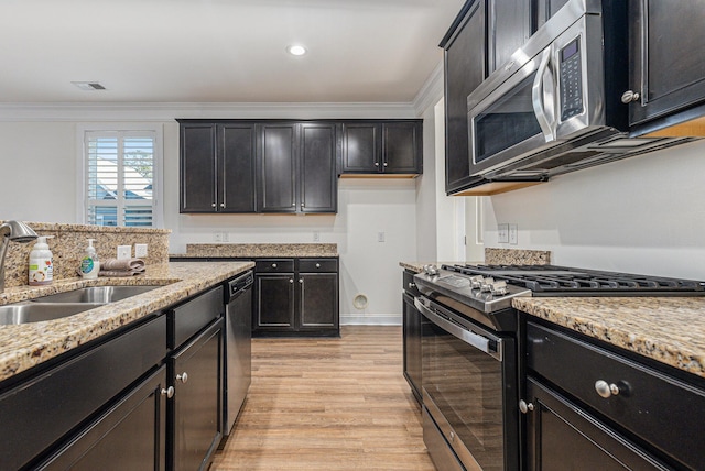 kitchen featuring appliances with stainless steel finishes, sink, ornamental molding, light wood-type flooring, and light stone counters