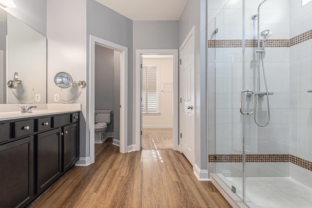 bathroom with hardwood / wood-style floors, toilet, a shower with shower door, and vanity