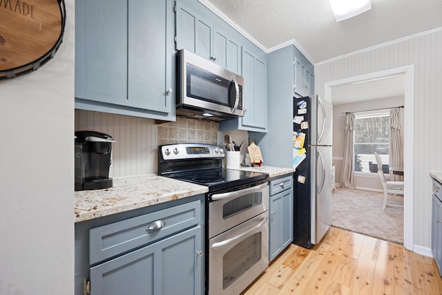 kitchen with ornamental molding, a textured ceiling, appliances with stainless steel finishes, light hardwood / wood-style floors, and light stone counters