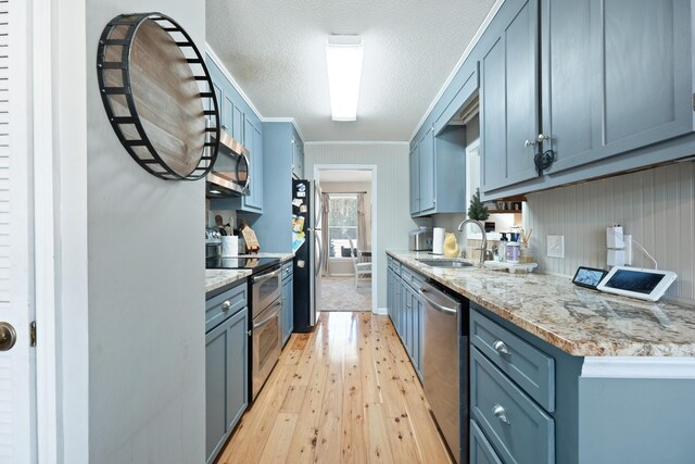 kitchen with light stone countertops, sink, light hardwood / wood-style floors, a textured ceiling, and appliances with stainless steel finishes