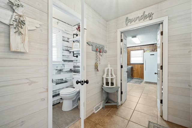 bathroom featuring wood walls, tile patterned flooring, a textured ceiling, and toilet