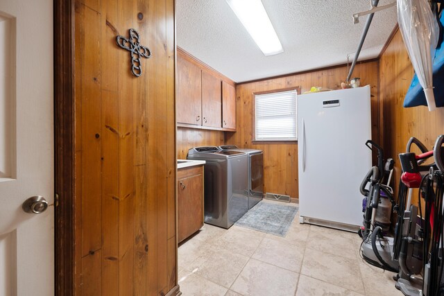 laundry room featuring wood walls, cabinets, independent washer and dryer, a textured ceiling, and ornamental molding