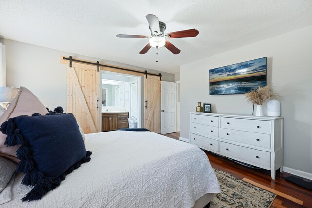 bedroom featuring ensuite bathroom, dark hardwood / wood-style floors, a barn door, ceiling fan, and a textured ceiling