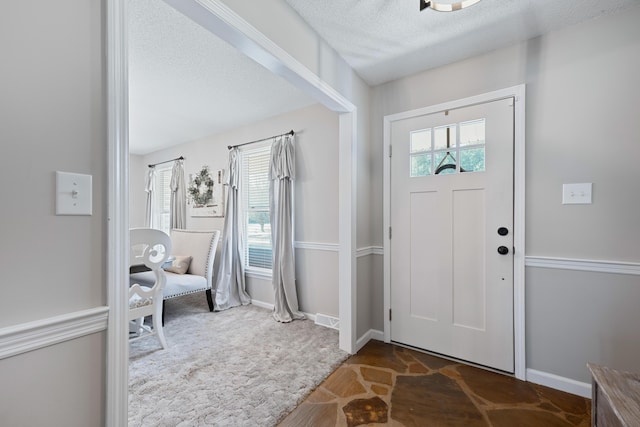 foyer entrance featuring plenty of natural light, a textured ceiling, and dark colored carpet