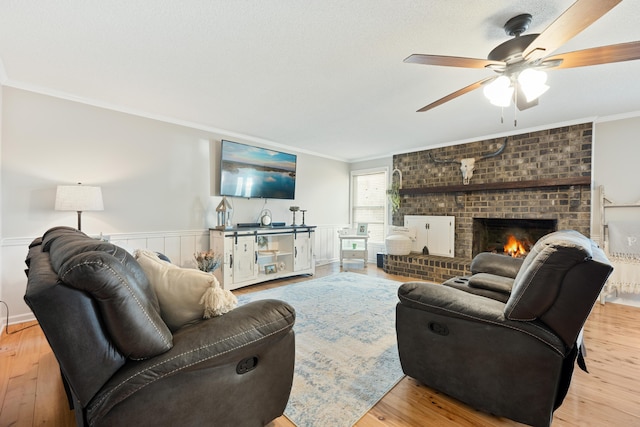 living room with crown molding, ceiling fan, light hardwood / wood-style floors, and a brick fireplace